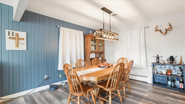 dining room with dark hardwood / wood-style floors, a baseboard radiator, and wooden walls