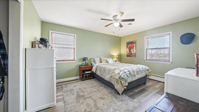 bedroom with hardwood / wood-style flooring, baseboard heating, and ceiling fan