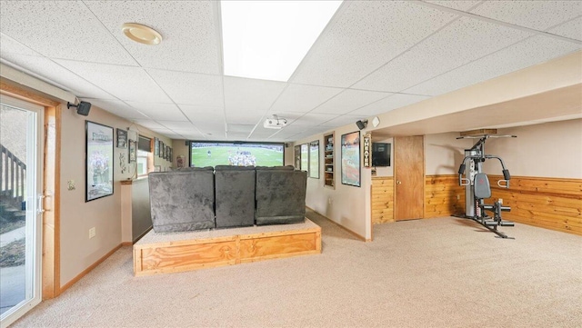 interior space with a drop ceiling, carpet floors, and wooden walls