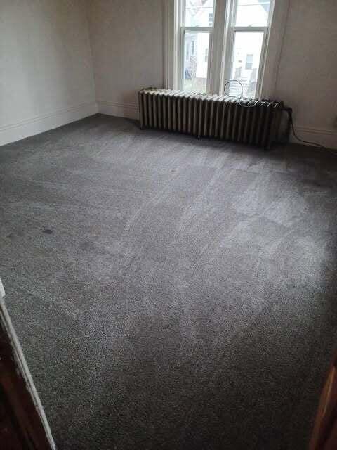 unfurnished room with dark carpet and radiator heating unit