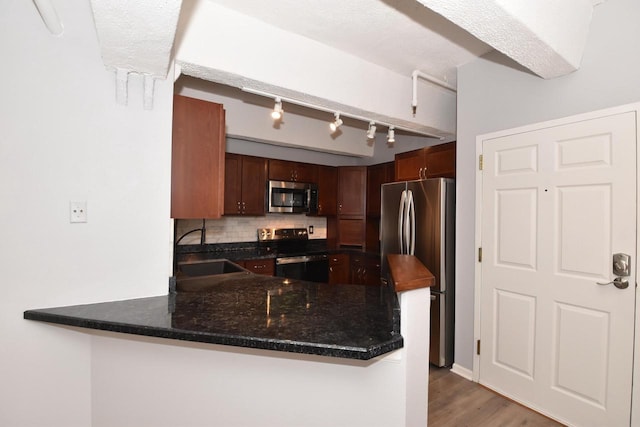 kitchen featuring sink, kitchen peninsula, decorative backsplash, wood-type flooring, and stainless steel appliances