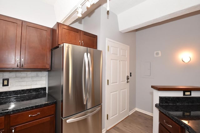 kitchen with stainless steel fridge, backsplash, hardwood / wood-style flooring, and dark stone counters