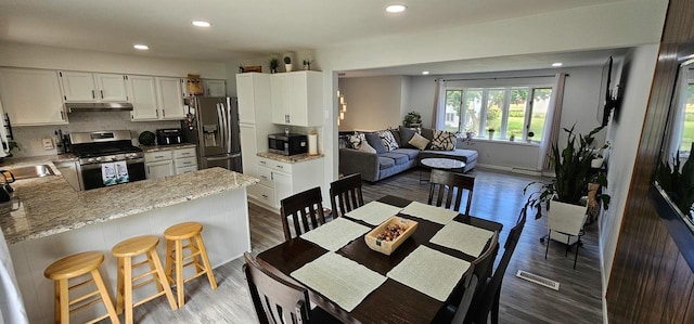 interior space with a breakfast bar, backsplash, hardwood / wood-style flooring, appliances with stainless steel finishes, and kitchen peninsula