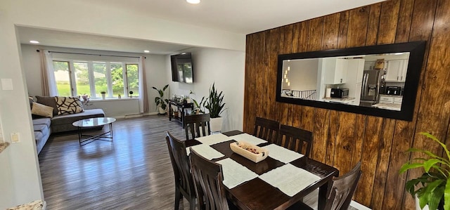 dining space with wooden walls and dark wood-type flooring