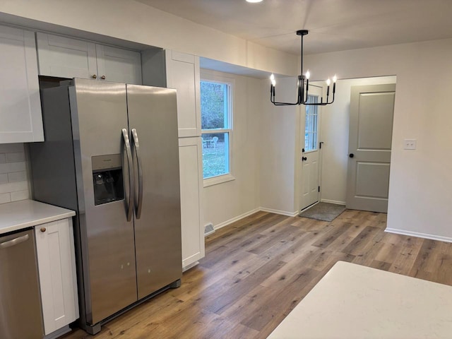 kitchen with backsplash, white cabinetry, stainless steel appliances, and decorative light fixtures