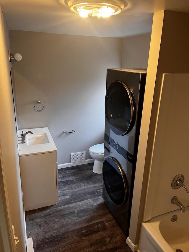 full bathroom with stacked washing maching and dryer, washtub / shower combination, wood-type flooring, toilet, and vanity