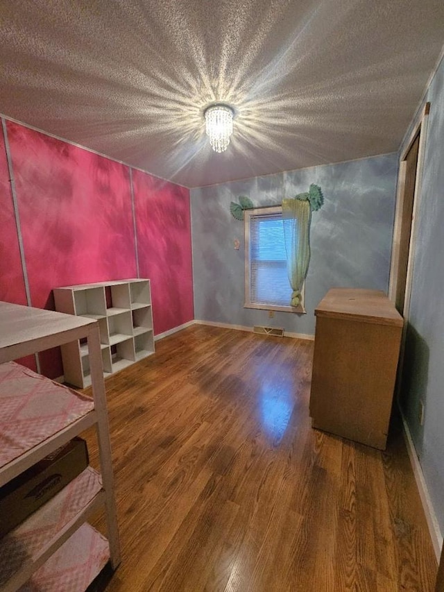 bedroom with hardwood / wood-style floors, a textured ceiling, and an inviting chandelier