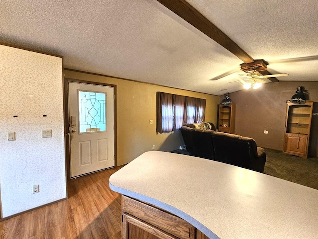 interior space with ceiling fan, beamed ceiling, wood-type flooring, and a textured ceiling