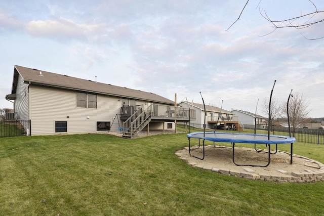 rear view of property with a lawn, a trampoline, and a wooden deck