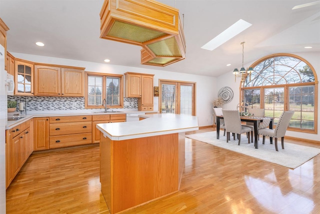 kitchen featuring a kitchen island, vaulted ceiling with skylight, decorative light fixtures, sink, and light hardwood / wood-style floors