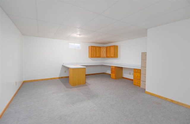 unfurnished office featuring built in desk, light colored carpet, and a drop ceiling