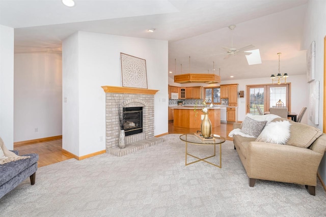 living room with high vaulted ceiling, a skylight, light colored carpet, ceiling fan, and a brick fireplace