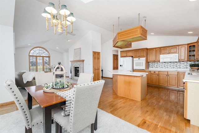 dining space with a brick fireplace, a chandelier, high vaulted ceiling, and light hardwood / wood-style flooring