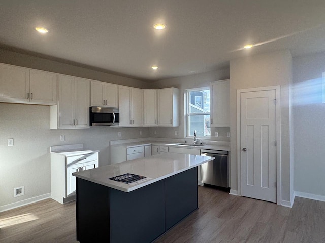 kitchen with hardwood / wood-style floors, sink, appliances with stainless steel finishes, a kitchen island, and white cabinetry