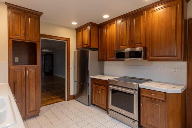 kitchen featuring tile countertops, sink, light wood-type flooring, and stainless steel appliances