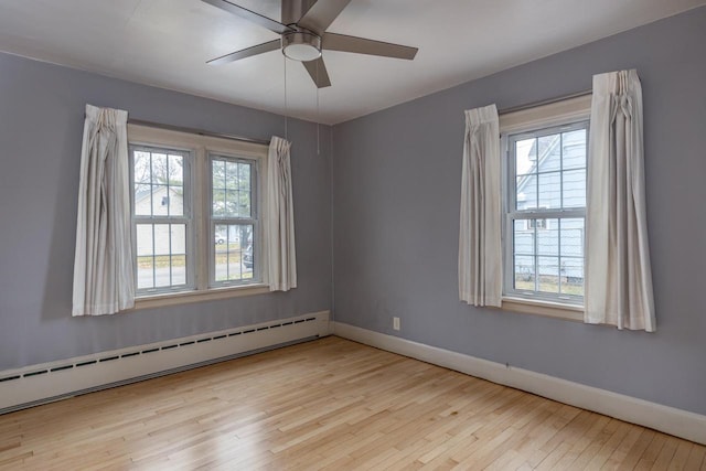 empty room with a wealth of natural light, light hardwood / wood-style flooring, ceiling fan, and a baseboard heating unit