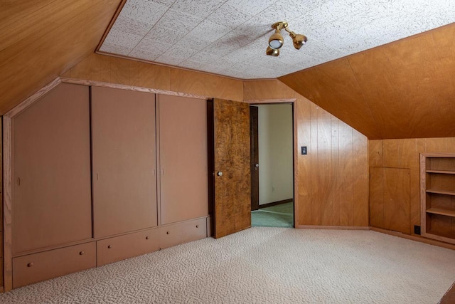 additional living space featuring built in shelves, wood walls, light carpet, and vaulted ceiling