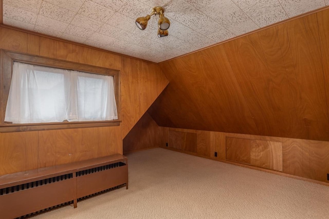 additional living space featuring light carpet, lofted ceiling, radiator, and wooden walls