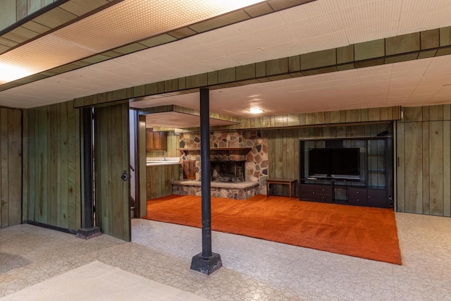 basement featuring carpet, wood walls, and a stone fireplace