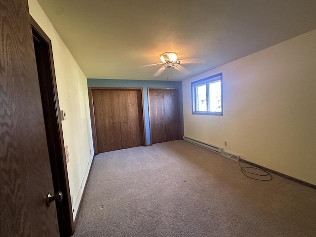 unfurnished bedroom with carpet flooring, a baseboard radiator, ceiling fan, and multiple closets