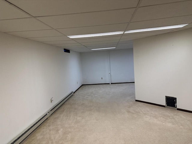 empty room with light carpet, a drop ceiling, and a baseboard heating unit