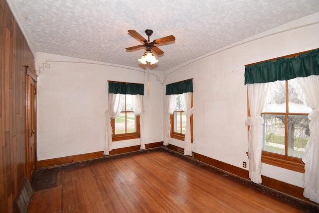 empty room featuring wooden walls, vaulted ceiling, ceiling fan, a textured ceiling, and dark hardwood / wood-style flooring