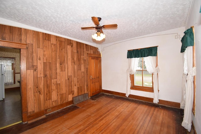 spare room featuring a textured ceiling, dark hardwood / wood-style floors, ceiling fan, and wooden walls