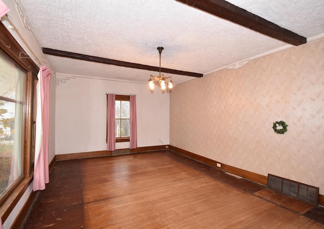 spare room with a notable chandelier, beamed ceiling, a textured ceiling, and hardwood / wood-style flooring