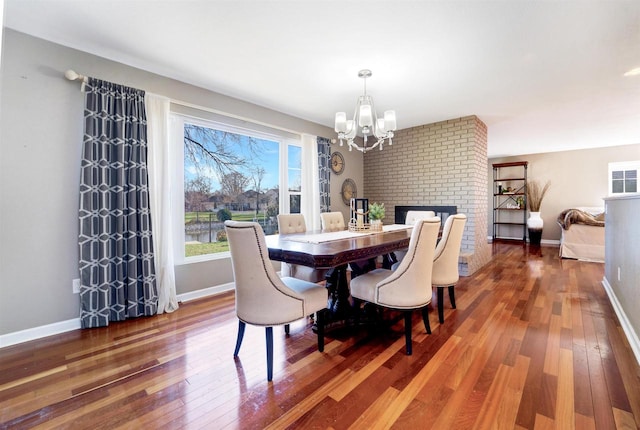 dining area with hardwood / wood-style flooring, a notable chandelier, and a brick fireplace