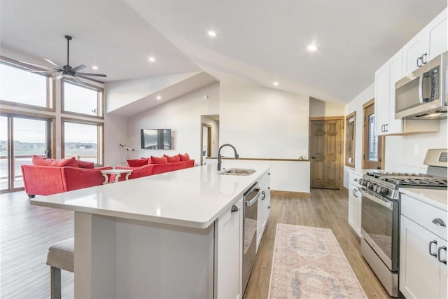 kitchen with a center island with sink, white cabinets, sink, light hardwood / wood-style flooring, and appliances with stainless steel finishes