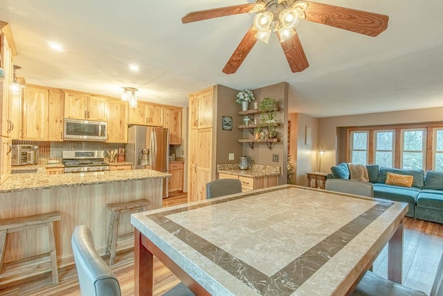 kitchen featuring ceiling fan, light wood-type flooring, light brown cabinetry, appliances with stainless steel finishes, and a breakfast bar area