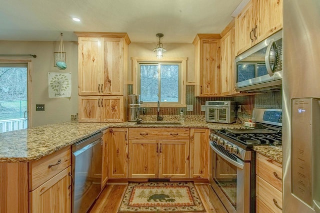 kitchen with sink, hanging light fixtures, kitchen peninsula, appliances with stainless steel finishes, and light wood-type flooring