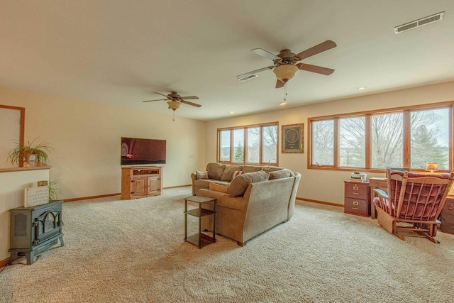 carpeted living room featuring ceiling fan and a wood stove