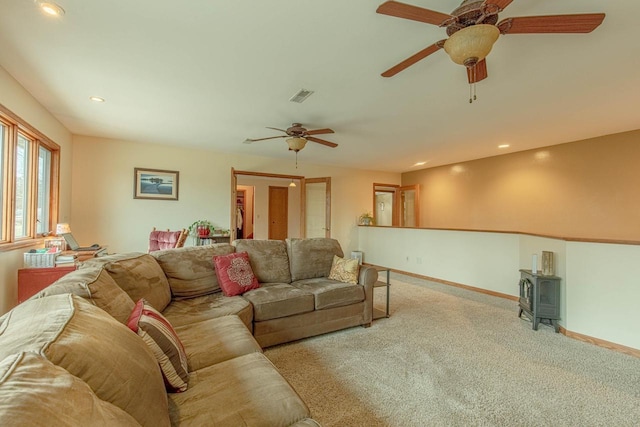 carpeted living room with a wood stove and ceiling fan