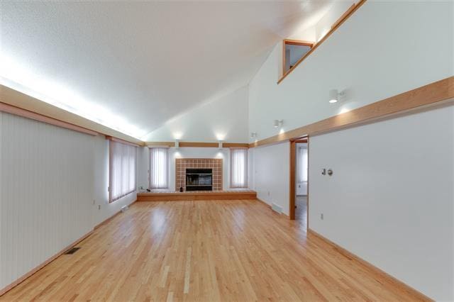 unfurnished living room featuring wood walls, a fireplace, high vaulted ceiling, and light hardwood / wood-style flooring