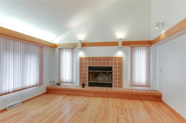 unfurnished living room featuring a tile fireplace, hardwood / wood-style floors, and vaulted ceiling