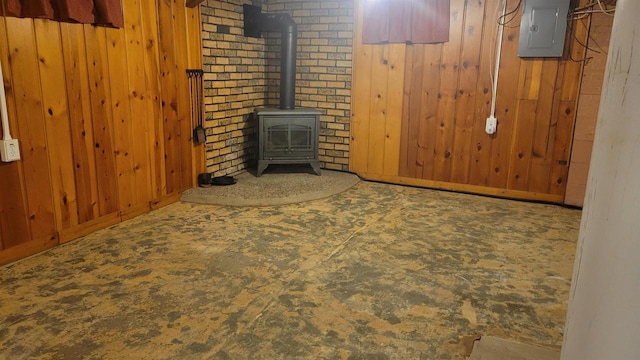 unfurnished living room with electric panel, a wood stove, and wood walls