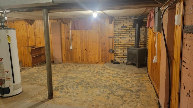 basement with a wood stove, wooden walls, and water heater