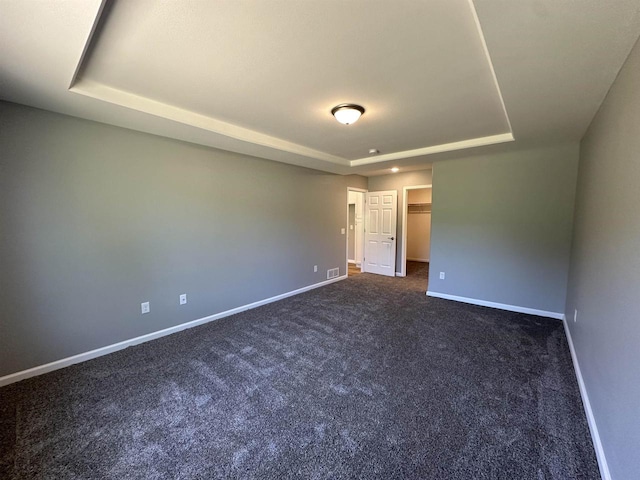 spare room with dark colored carpet and a raised ceiling