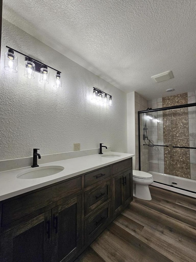 bathroom featuring vanity, toilet, a textured ceiling, an enclosed shower, and wood-type flooring