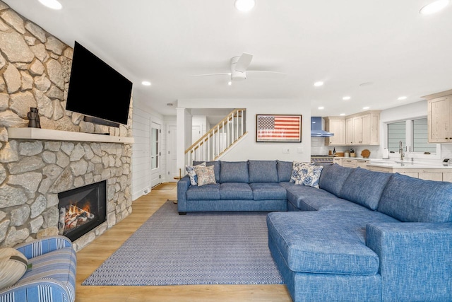 living room with light hardwood / wood-style flooring, ceiling fan, a stone fireplace, and sink