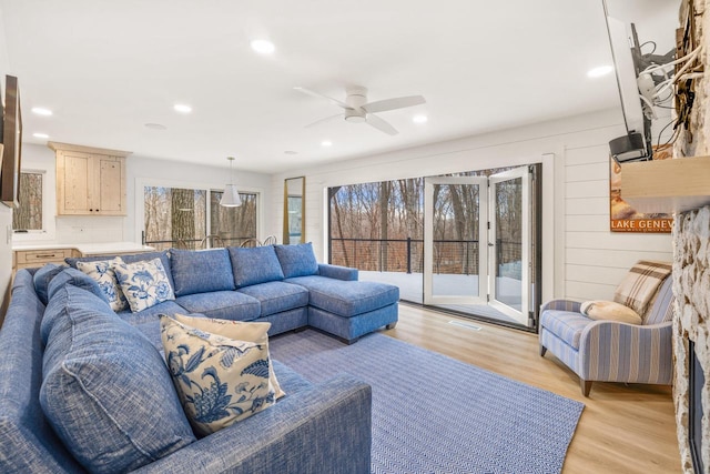 living room with ceiling fan, light hardwood / wood-style flooring, and wooden walls