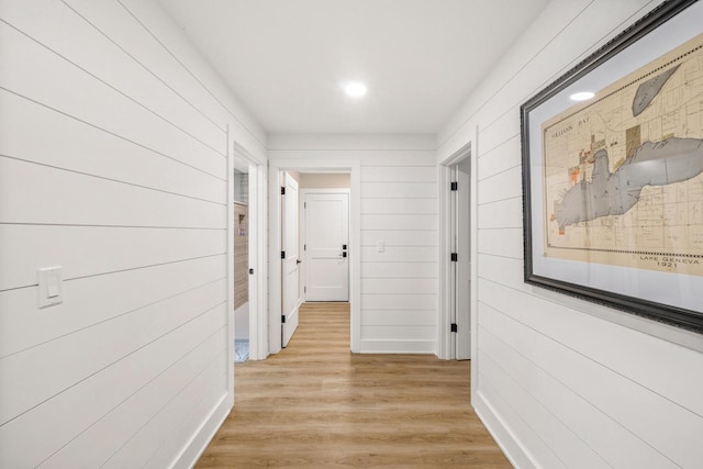 hallway with light hardwood / wood-style flooring and wood walls