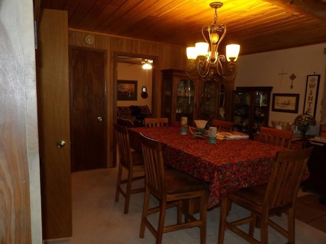 carpeted dining area featuring ceiling fan with notable chandelier, wood walls, and wood ceiling