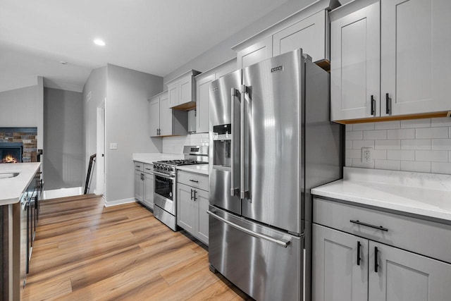 kitchen featuring a stone fireplace, gray cabinets, appliances with stainless steel finishes, tasteful backsplash, and light hardwood / wood-style floors