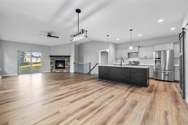 kitchen with stainless steel appliances, an island with sink, pendant lighting, white cabinets, and light wood-type flooring