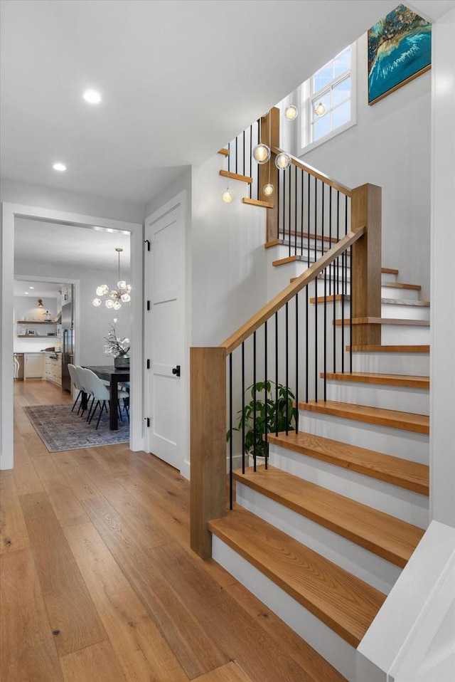 stairs featuring wood-type flooring and an inviting chandelier