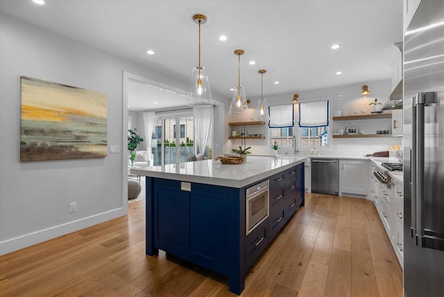 kitchen featuring hanging light fixtures, stainless steel appliances, a kitchen island, light hardwood / wood-style flooring, and white cabinets