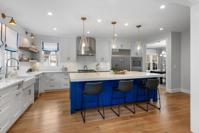 kitchen with white cabinets, wall chimney exhaust hood, plenty of natural light, and stainless steel appliances