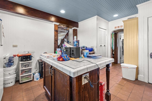 kitchen featuring tile countertops, light tile patterned floors, ornamental molding, beamed ceiling, and dark brown cabinetry